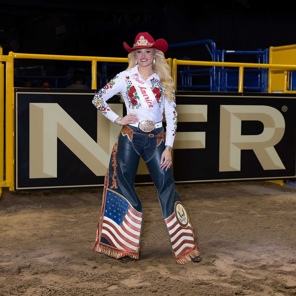 Miss Rodeo America, Callie Mueller, wearing a white button-down shirt, red hat, and chaps, posing in the arena at the National Finals Rodeo.